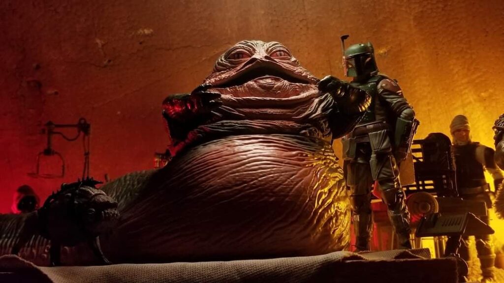 Jabba the Hutt seduto nel suo palazzo accanto al cacciatore di taglie Boba Fett in una scena dell’universo Star Wars.